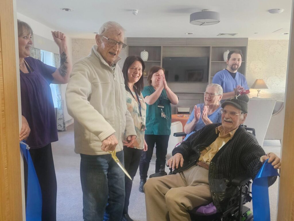 resident cutting a blue ribbon to celebrate opening of dementia community